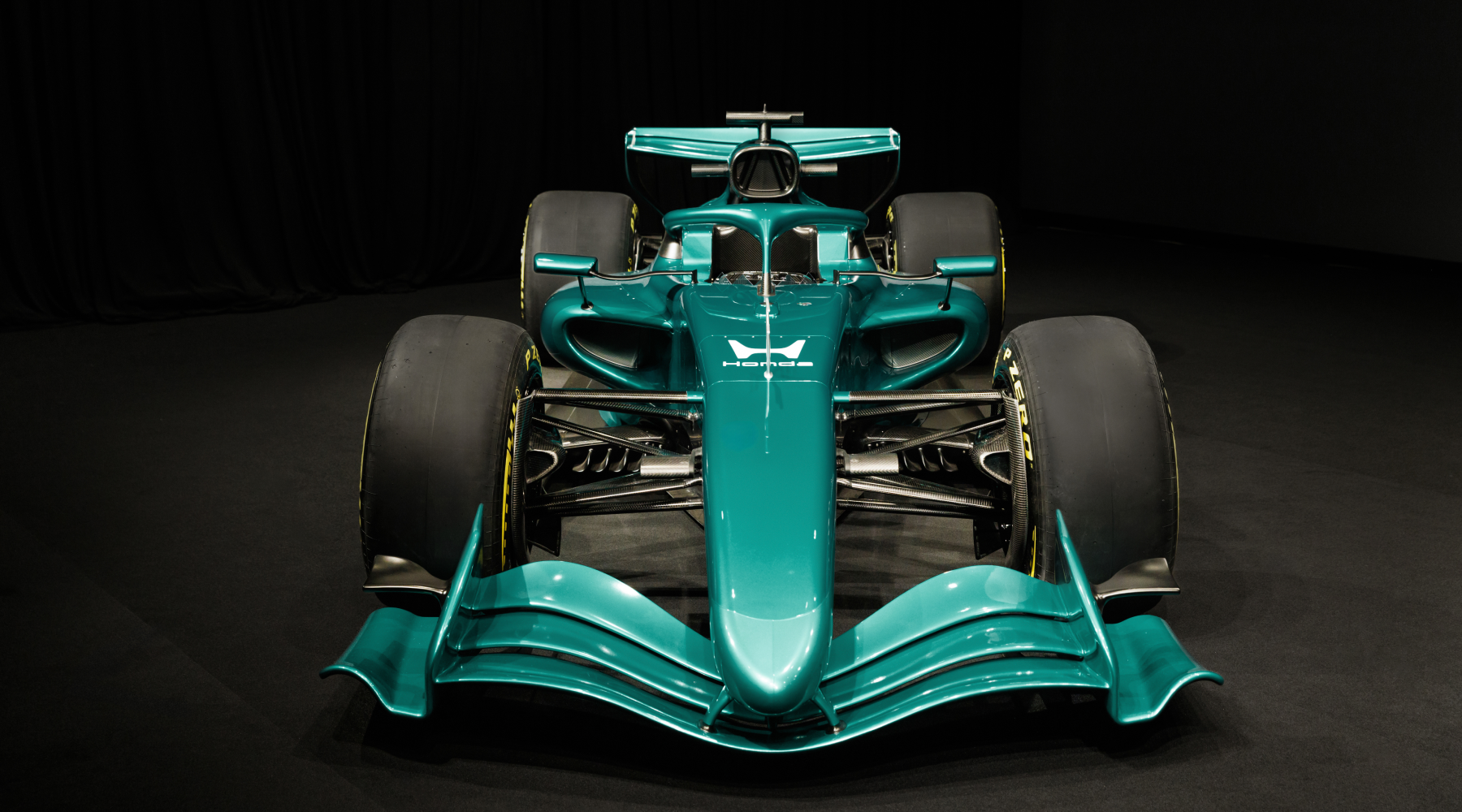 Front view of a turquoise Formula 1 racing car against a black background. The sleek aerodynamic design features a prominent front wing, large tires, and intricate suspension components visible beneath the bodywork.